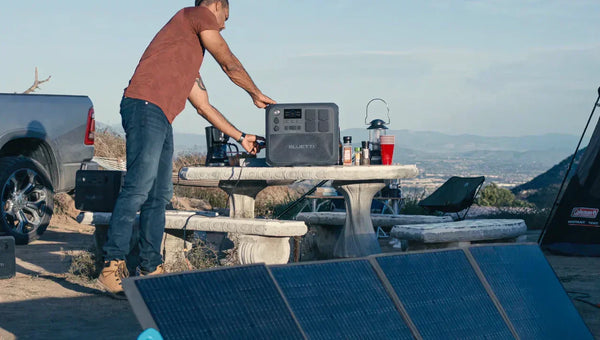 A man is using a Bluetti Elite 100V2 to power other devices on an outdoor camping table.