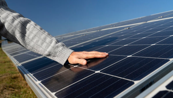 Mão de homem sobre placas de energia solar, céu azul ao fundo